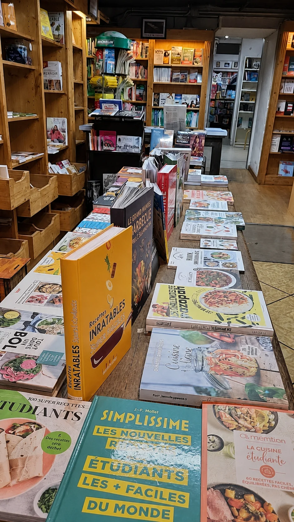 Une longue table de livres de cuisine entre les rayonnages en bois